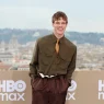 Nam diễn viên Tom Blyth mỉm cười trên thảm đỏ sự kiện HBO Max, diện áo sơ mi túi hộp màu xanh olive phối cùng cà vạt lụa vàng đồng theo phong cách stealthy tie-tuck, kết hợp với quần tây ống rộng màu nâu đậm.